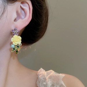 Close-up of floral earrings with purple crystals, yellow rose, and light blue pearl drops
