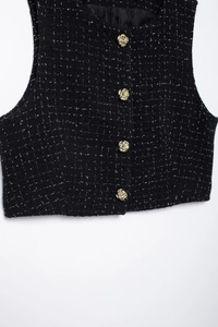 Détail d'un gilet en tweed noir avec des boutons en métal doré en forme de rose sur blanc