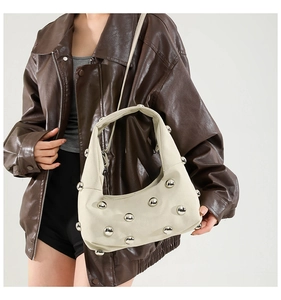 Detail of off-white tote bag with silver studs worn with a brown leather jacket