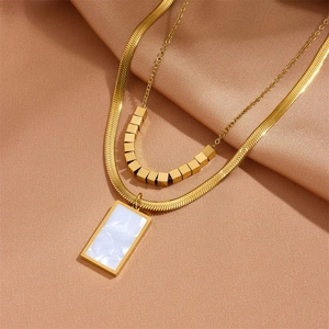 Detail of double-layered gold necklace with square beads and white marble pendant