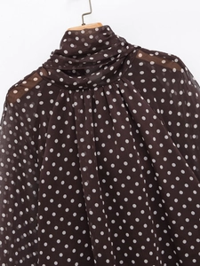Detail of high neck polka dot chiffon blouse featuring pleated collar and wooden hanger
