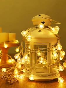 Close-up of warm white bubble LED string lights wrapped around a white vintage lantern