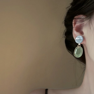Detail of elegant two-tone resin earrings in blue and green on model's ear