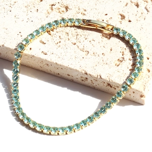 Detail of light blue square-cut tennis bracelet on white stone with gold plating