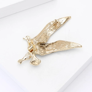 Detail of a golden alloy hummingbird brooch with textured wings on a white pedestal