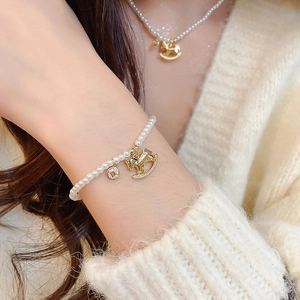 Close-up of pearl bracelet and necklace with golden rocking horse charms on beige sweater