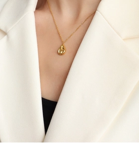 Polished gold teardrop pendant necklace worn over a minimalist white blazer suit