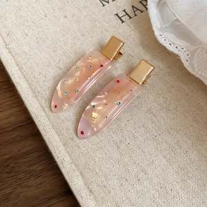 Detail of pink pearlescent hair clips with multi-colored rhinestones on linen fabric