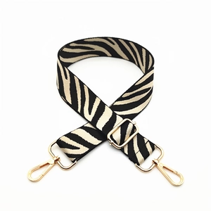 Macro view of adjustable zebra print canvas bag strap with shiny gold metal buckles