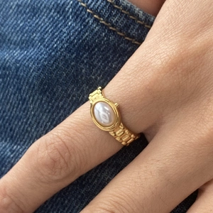 Detailansicht eines goldenen Gliederarmband-Rings mit ovaler Perle am Finger getragen