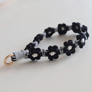 Macro shot of hand-woven daisy lanyard with black, grey, white yarn and metal clasp