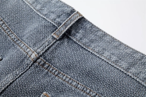 Detailed close-up of high-density herringbone denim weave and gray-blue stitching