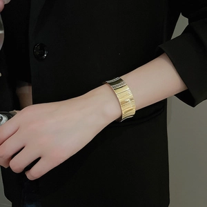 Detail of wide golden textured cuff bracelet worn with a minimalist black blazer sleeve