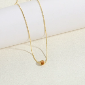 Minimalist gold necklace with hollow spherical pendant on a white pedestal