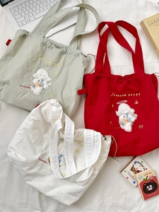 Embroidered canvas tote bag with drawstring closure in multiple colors on white background