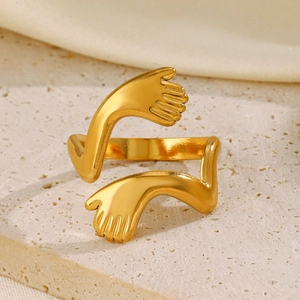 Minimalist gold hugging hands open ring displayed on beige stone with silk texture