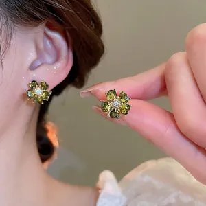 Elegant emerald green flower stud earrings with diamonds worn on a female model's ear
