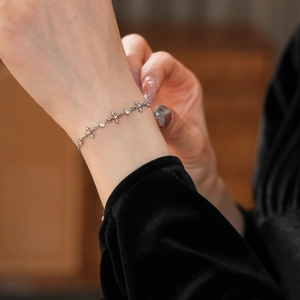 Detailed view of zircon cross bracelet in silver finish worn on wrist with black sleeve