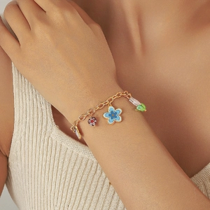 Bracelet chaîne doré avec fleur bleue dégradée et pendentifs en forme de cœur au poignet