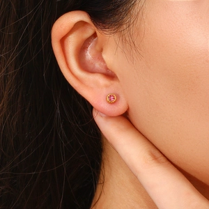 Close-up of gold stud earring with pink gemstone on model ear showing intricate details