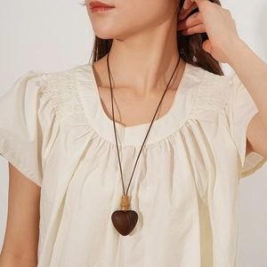 Close-up of a heart-shaped wooden pendant necklace worn by a model in white clothing