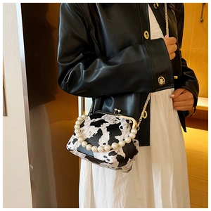 Detail of a cow print crossbody bag featuring a pearl handle and vintage kiss-lock closure