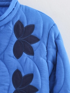 Detailed view of blue quilted jacket featuring intricate leaf applique embroidery