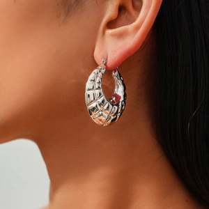 Detail view of silver geometric hoop earrings with a quilted metallic texture on a model