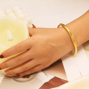 Close-up of minimalist polished gold stainless steel bangle worn on a wrist in warm lighting