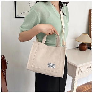 Close-up of cream corduroy handbag featuring a retro woven strap and small brand patch