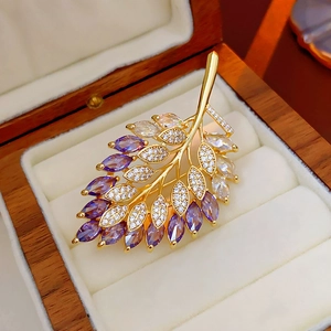 Close-up of golden leaf brooch with purple and clear zircons on a wooden jewelry box