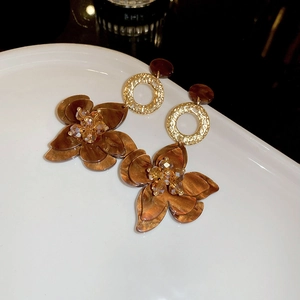 Close-up of amber acetate flower earrings with champagne crystals on a white ceramic plate