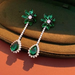 Macro shot of silver zircon flower earrings with emerald green teardrop pendant