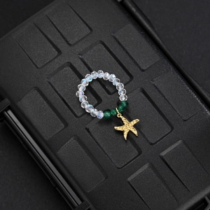Detailed macro of gold starfish pendant with green beads and clear crystal elastic ring