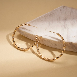 Detail of gold geometric C-shaped hoop earrings with faceted prism surface on marble
