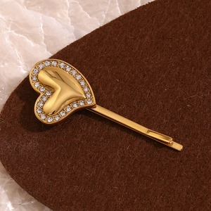 Macro shot of gold heart hair clip with sparkling rhinestones on textured surface