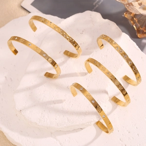 Macro detail of gold-plated stainless steel bangles with star, moon, and shell engravings