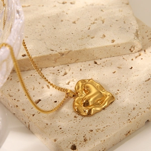 Macro shot of gold heart pendant with liquid metal design on a beige stone