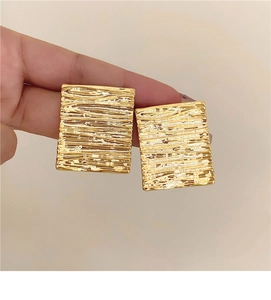 Detailed view of golden rectangular earrings with fine horizontal water-ripple texture