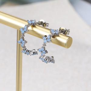 Macro view of blue zircon flower earrings with silver C-shape floral details on a gold stand