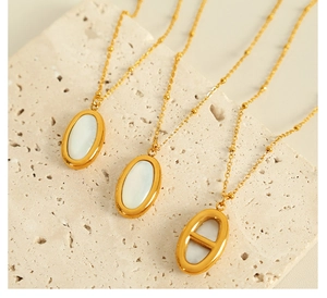 Macro detail of oval white shell pendants with golden chains on beige stone