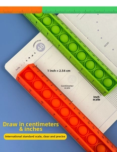 Detail of green and orange silicone pop-it rulers showing cm and inch scales on blue background