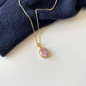 Close-up of gold necklace with oval pink gemstone and shimmering pavé diamond halo