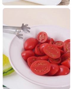 Macro shot of stainless steel palm-shaped food clip picking up a fresh tomato slice