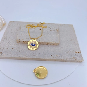 Detail view showing the blue Evil Eye pendant and smooth gold-plated back on stone slabs