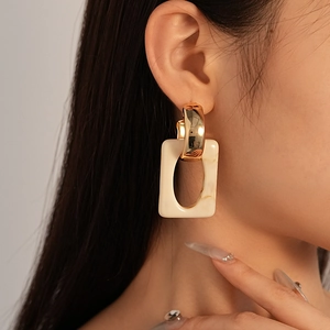 Detail of geometric resin rectangle earrings with gold finish on a model