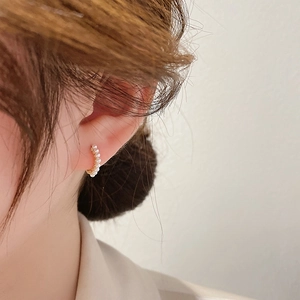 Minimalist gold hoop earrings featuring delicate white pearls worn by a model in profile view
