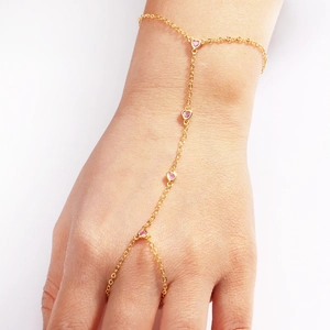 Close-up of 18k gold finger chain bracelet with four pink heart-shaped gemstones