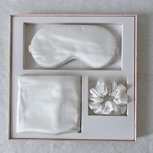 Macro shot of ivory satin sleep set including eye mask, pillowcase and scrunchie in gift box