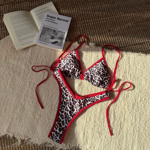 Flat lay of leopard print bikini with red trim ties on textured beach towel and mat